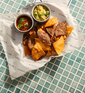 Chips, salsa, and guacomole in a lined basket on a blue tile