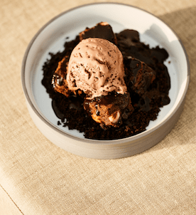 Brownie in a white dish with scoop of chocolate ice cream