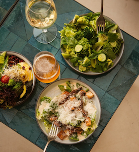 Three different salads on a green placemat with two glasses of wine