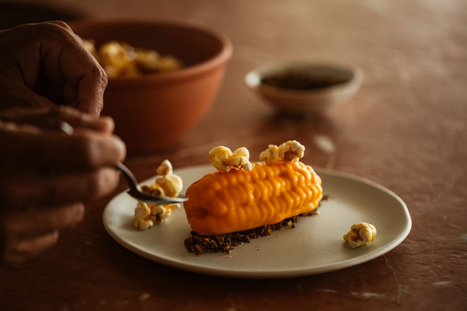 Small piece of corn on a grey round small plate sitting on a dark tabletop with other bowls in the background