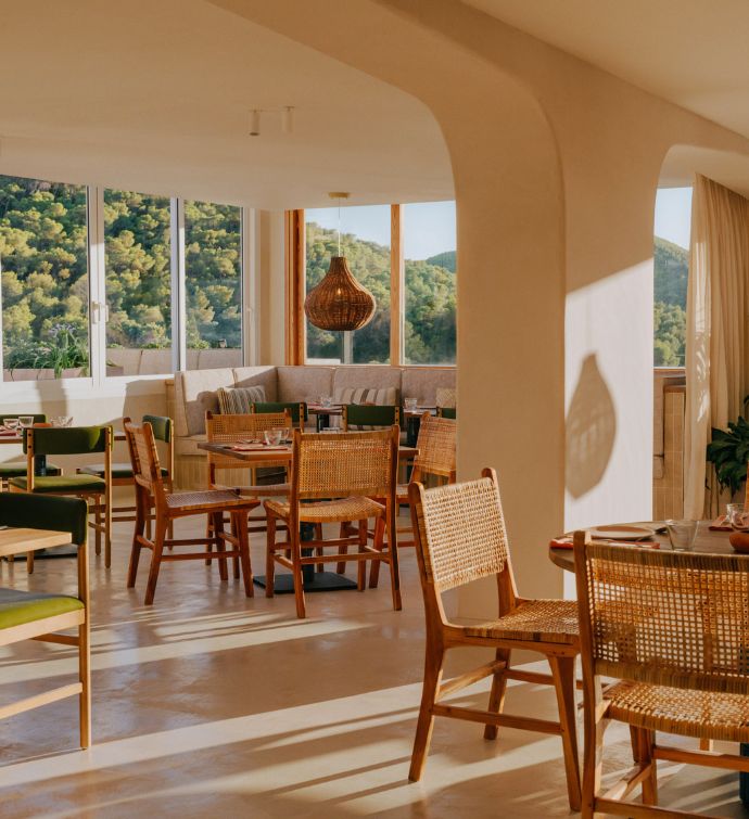 Sun-drenched dining room with light wooden chairs and tables and windows looking out to tree-filled mountains