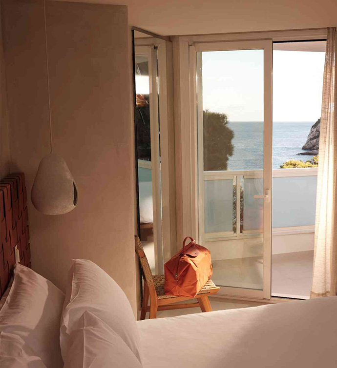 Dormitorio con cama y puerta de balcón con vistas al mar.