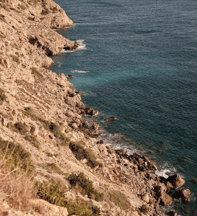 una ladera de playa rocosa que desemboca en aguas azul oscuro
