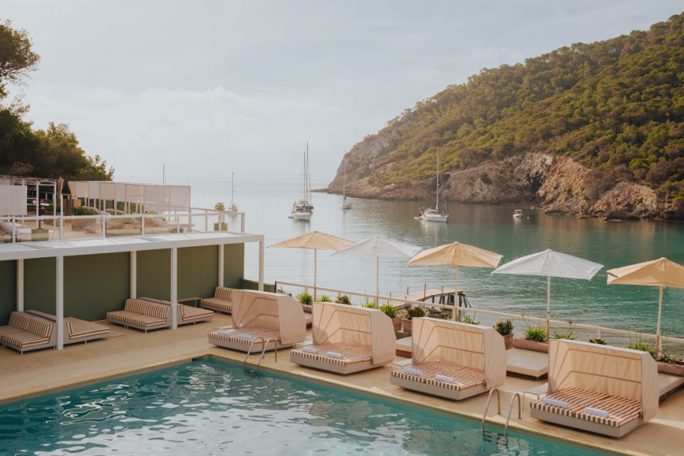 Pool with cabana lounges and striped umbrellas with an ocean and mountains in the background