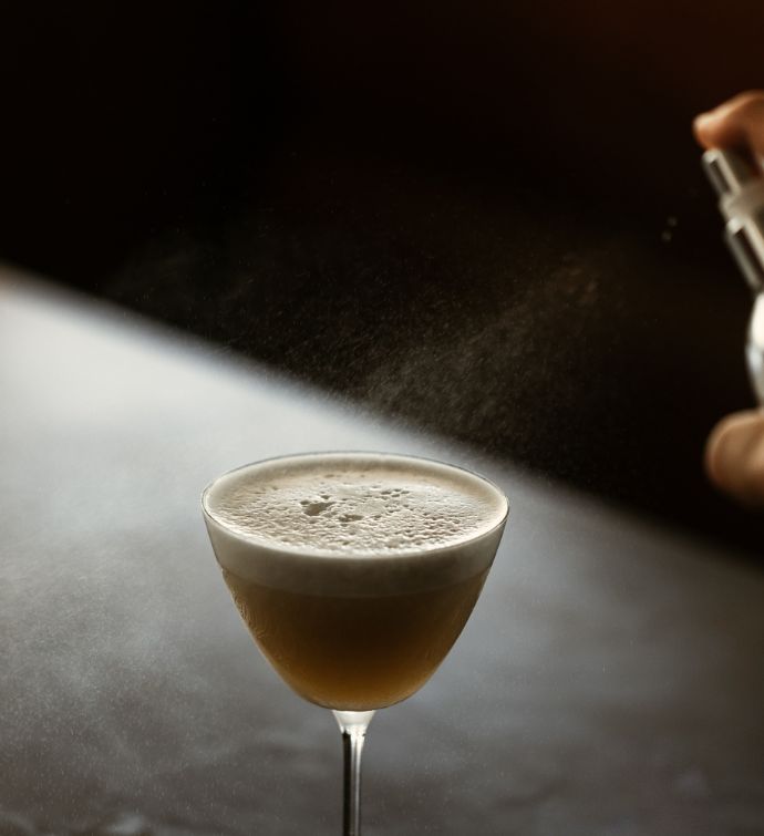 Close up image of small cocktail in martini glass with something being sprayed on top of it