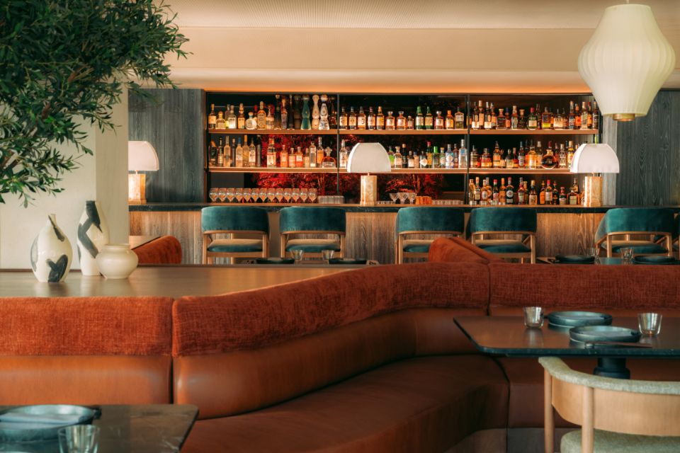 Dining room with burnt orange booth and wooden bar in the background with turqouise bar stools