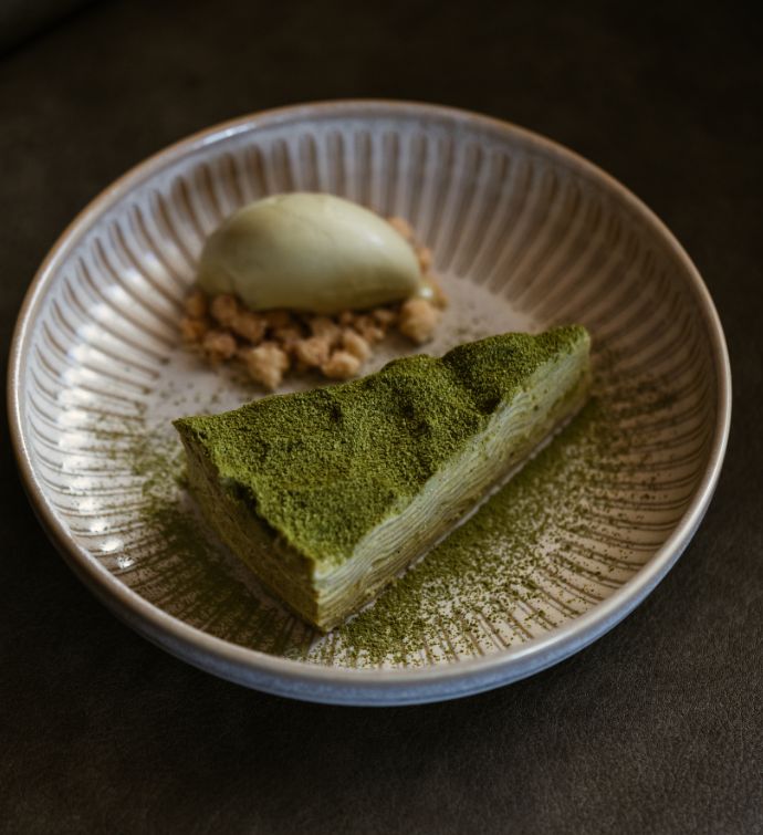 Green matcha cake with cream on the side on a white dish on a dark countertop