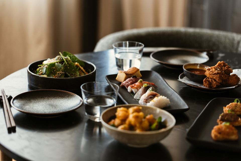 Plate of sushi and other small dishes on a black table with two glasses of water