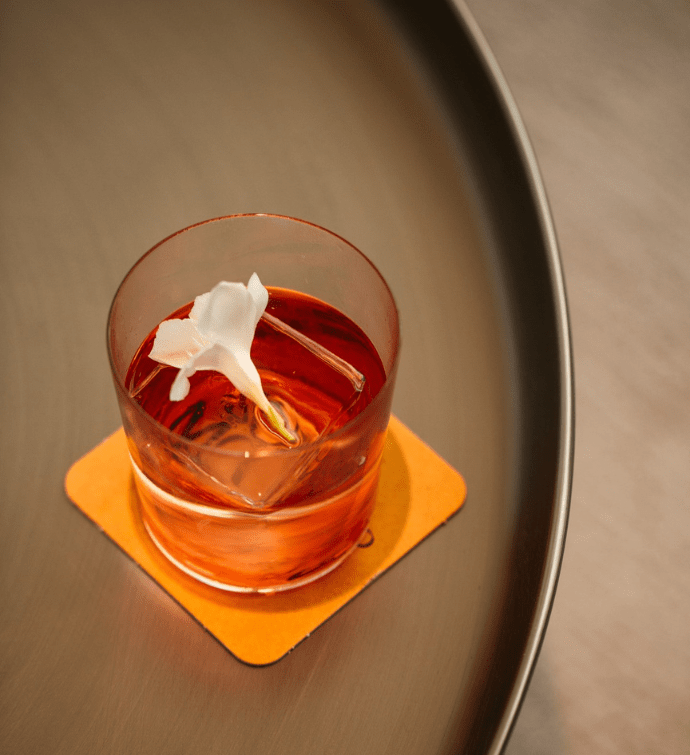 a pink cocktail in a small glass garnished with a white flower