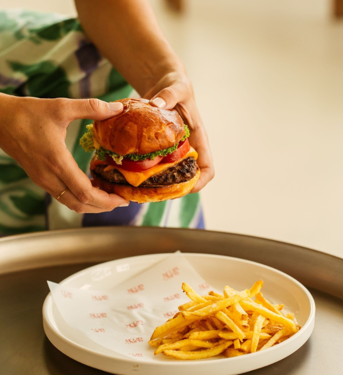 manos sosteniendo una gran hamburguesa en un plato con muchas patatas fritas 