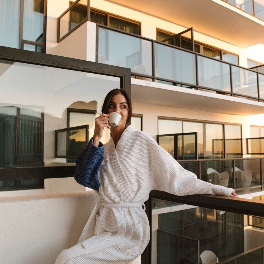 Woman in robe standing on her balcony drinking a cup of coffee