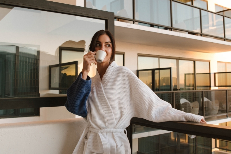 Woman in robe standing on her balcony drinking a cup of coffee