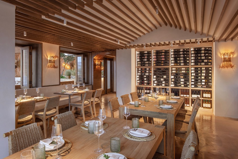 Interior del restaurante Casa Madera con largas mesas de madera y sillas de mimbre, y una pared con botellas de vino