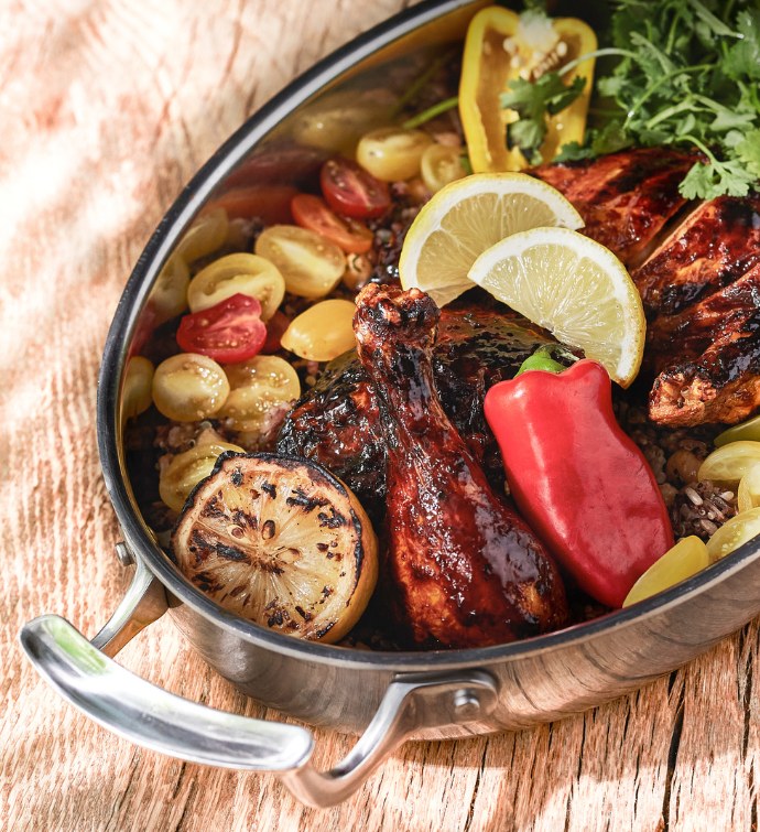 Plato de pollo asado con limones, tomates y pimientos en una sartén de metal