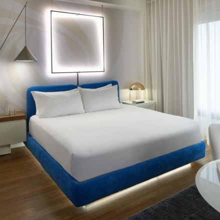 Large white bed with turqouise headboard in a sleek white hotel room