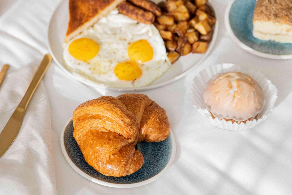 Desayuno con huevos, patatas, un cruasán y un bollo