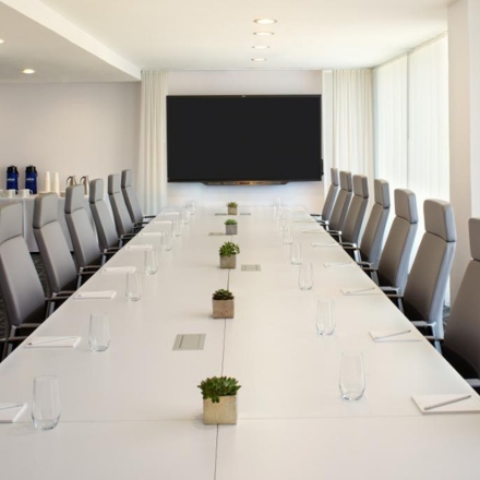 Sala de conferencias con mesa larga, sillas grises y televisor