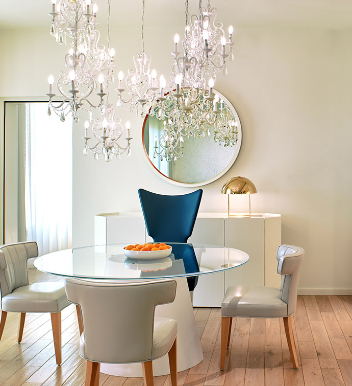 A dining room with a round table and chairs, a mirror and a chandelier.