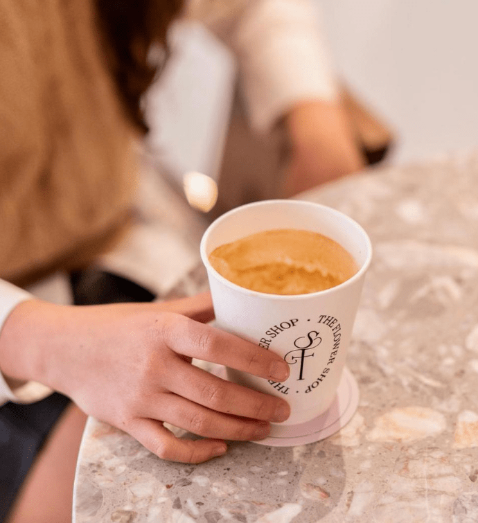 una mano sobre una mesa sosteniendo un café con leche en un vaso para llevar 