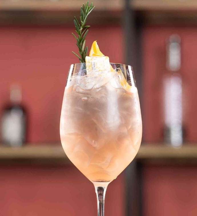 a light pink cocktail served in a white wine glass garnished with lemon