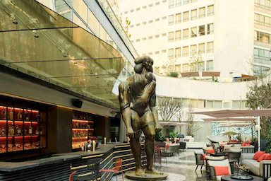 Large statue of a male figure in front of amodern building 