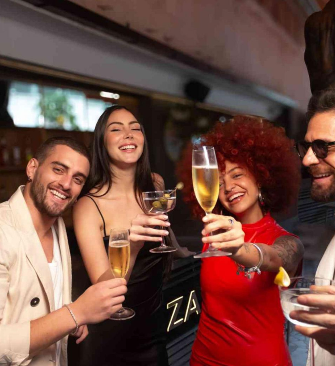 a group of men and women enjoying their cocktails, with a woman in red lifting her champagne glass