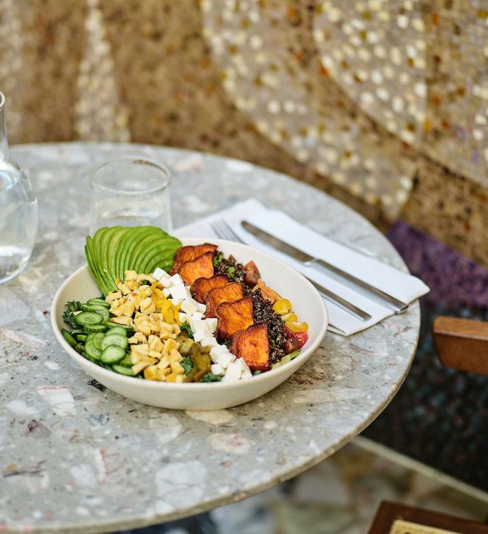 Chopped salad with vegetables, avocado, and cheese in a white bowl on a grey marbled table with silverware on a napkin to the side