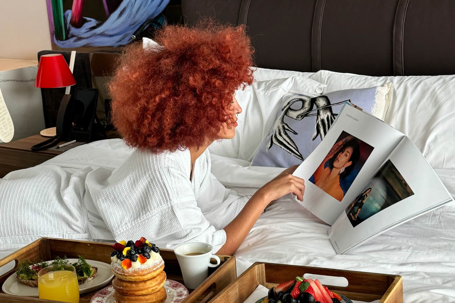 Mujer leyendo una revista en la cama con el desayuno en una bandeja