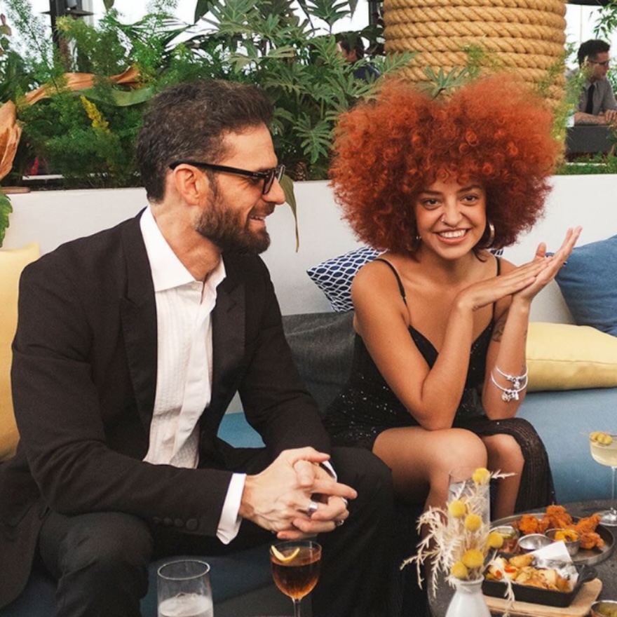 a couple enjoying themselves sitting on a rooftop terrace at a table with light bites and and drinks