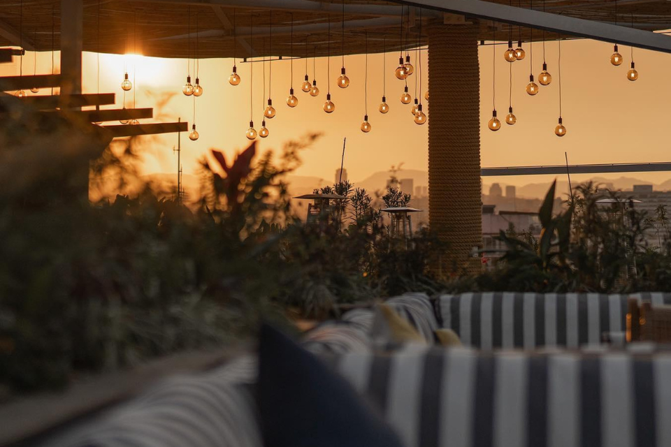 Outdoor terrace with sunset in the background and striped cushion seats in the foreground with roof overhead.