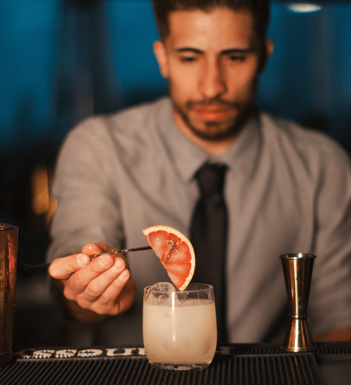 a bartender garnishing a cocktail with grapefruit