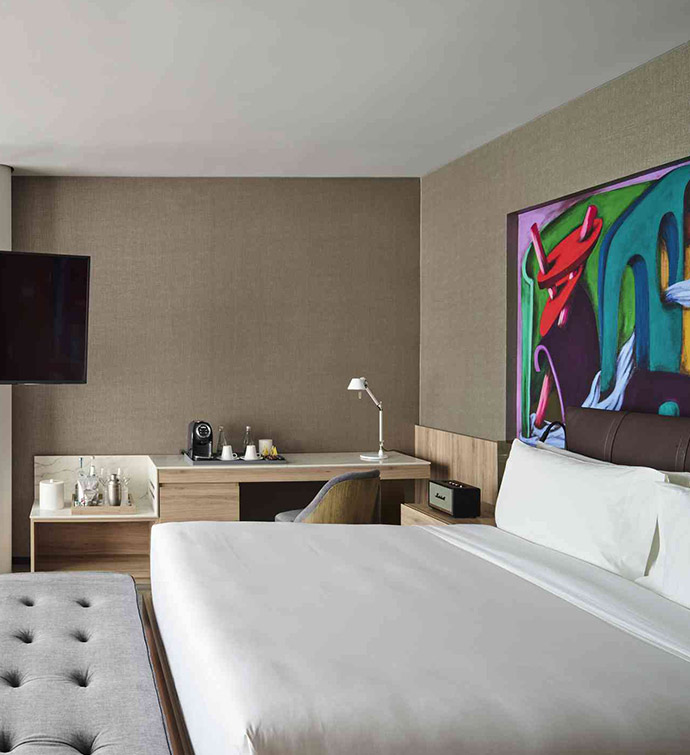 A hotel room with a cozy bed, a television, and a beautiful painting adorning the wall.