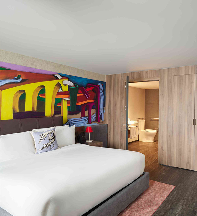 A hotel room with a large painting on the wall and bathroom.