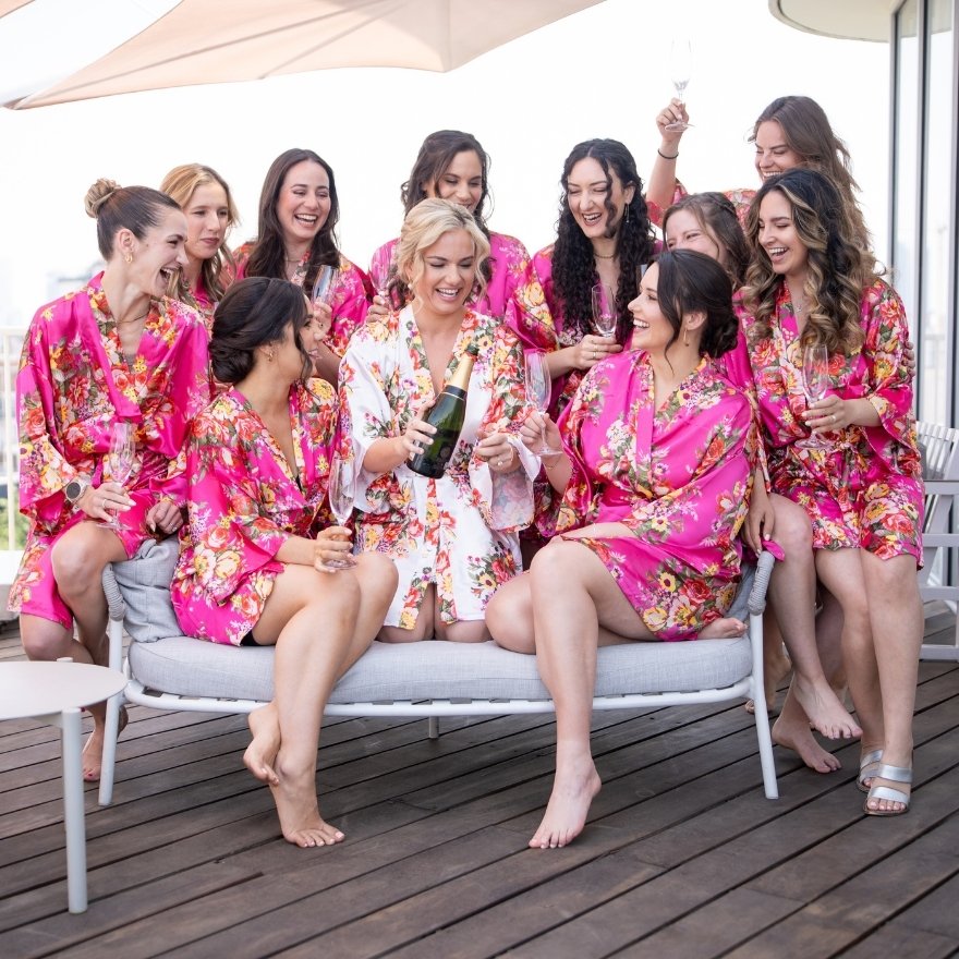 group of women in floral robes sitting and posing with a bottle of champagne