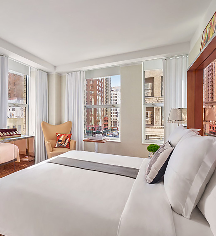 Interior of a hotel room featuring a bed, chair, and window.