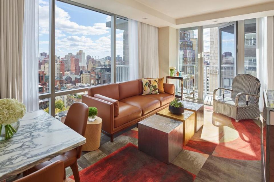 Hotel room with a leather couch, table and views of New York City