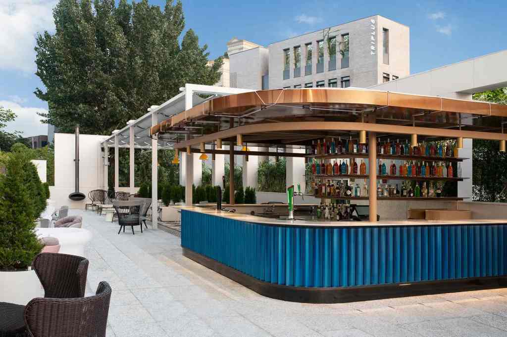 Free standing rectangular bar on a rooftop with blue tiles and a brass covering overhead with a white building in the background