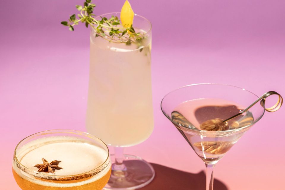 Three cocktails in various glasses with different garnishes on a purple background