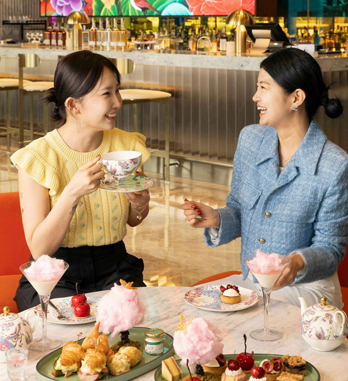 Two women laughing with each other and enjoying an afternoon tea spread in an upscale bar.