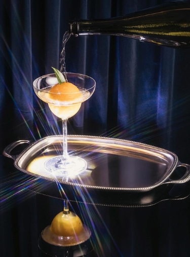 Cocktail with orange shape inside sits on a silver tray