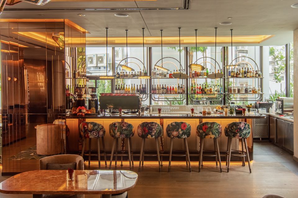 Modern warmly lit bar with floral bar stools, shelves of liquor, and gold decor accents