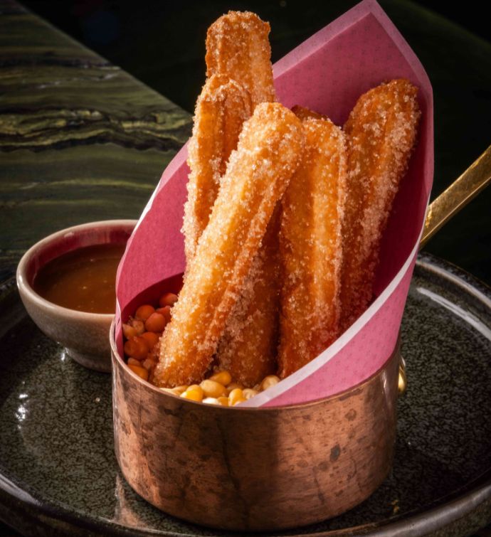 Churros in a silver bucket with dipping sauce on the side