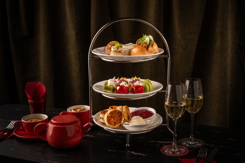 Tea tray with pastries and tea sandwiches with red pot of tea and tea cups and two glasses of champagne