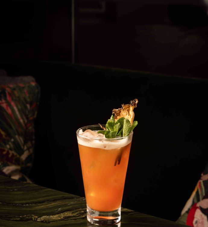 Orange cocktail in a tall glass with pineapple and green leaf garnish