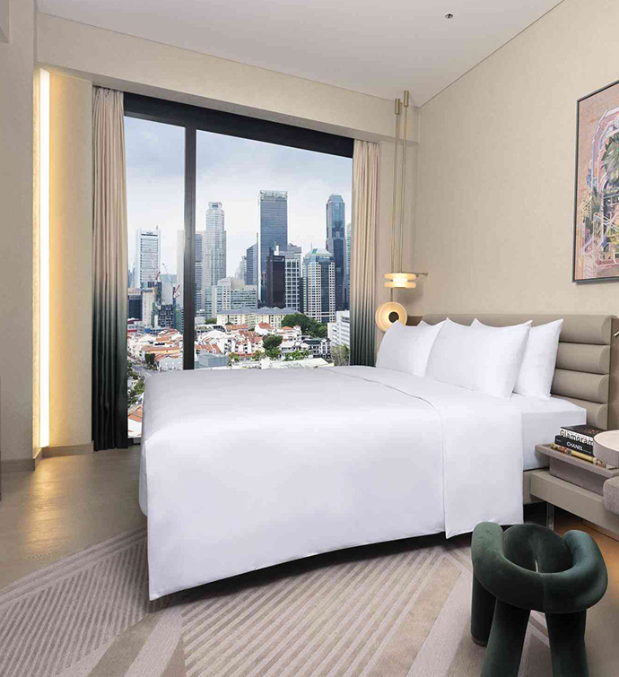 A spacious hotel room with a bed, a TV, a painting and a stunning city view from the window.