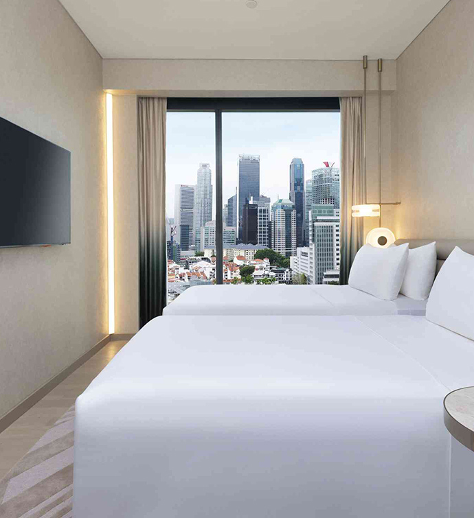 A hotel room with two beds, a TV and city view out the window.