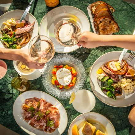 Multiple brunch dishes on a green tabletop with hands digging forks into plates of food