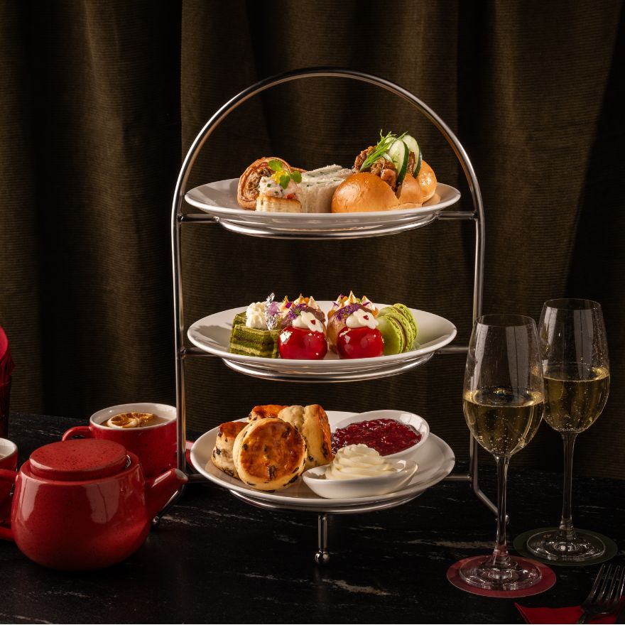 Tea tray with pastries and tea sandwiches with red pot of tea and tea cups and two glasses of champagne