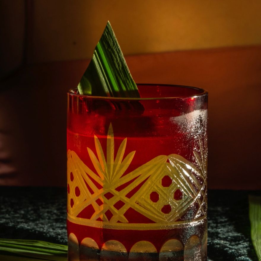 Cocktail in decorative glass with bamboo leaf sits on a dark bar