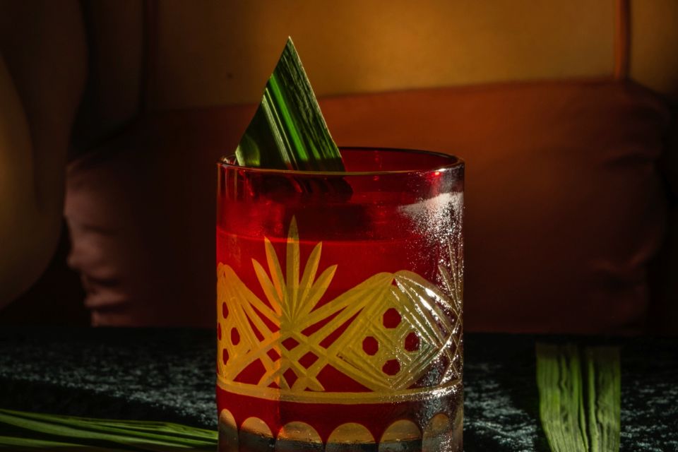 Cocktail in decorative glass with bamboo leaf sits on a dark bar